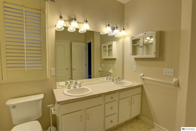 full bath with double vanity, a sink, toilet, and baseboards