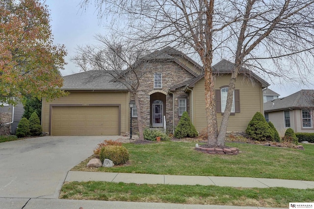 view of front facade featuring driveway, stone siding, roof with shingles, an attached garage, and a front yard