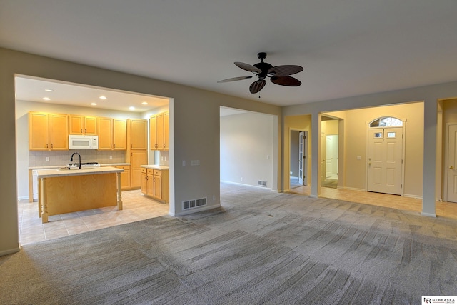 kitchen featuring light carpet, white microwave, visible vents, and light brown cabinetry