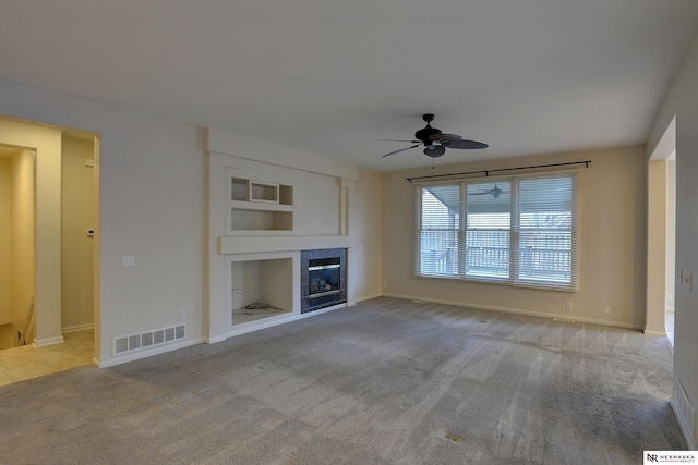 unfurnished living room with visible vents, ceiling fan, carpet floors, built in shelves, and a fireplace