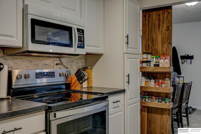 kitchen featuring stainless steel electric range oven, white microwave, dark countertops, and white cabinets