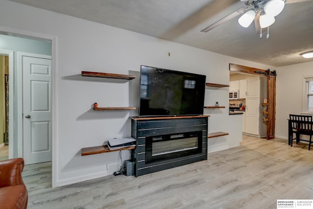 living area featuring baseboards, a barn door, a ceiling fan, and light wood-style floors