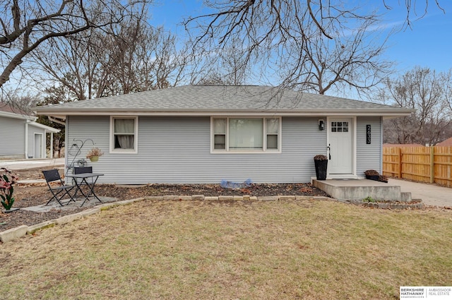 exterior space featuring a shingled roof, fence, and a lawn