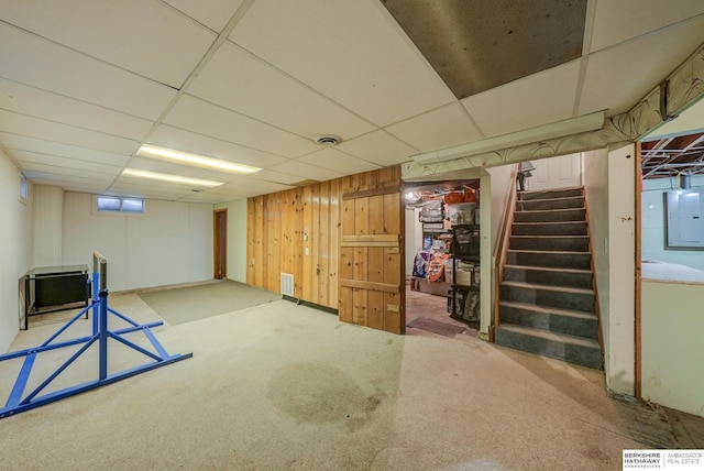 finished below grade area featuring stairs, a paneled ceiling, carpet, and electric panel