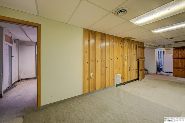 finished below grade area with visible vents, a paneled ceiling, wood walls, and freestanding refrigerator