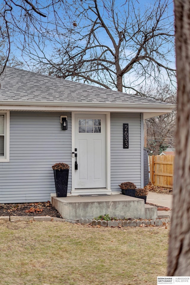 entrance to property with a shingled roof, a lawn, and fence