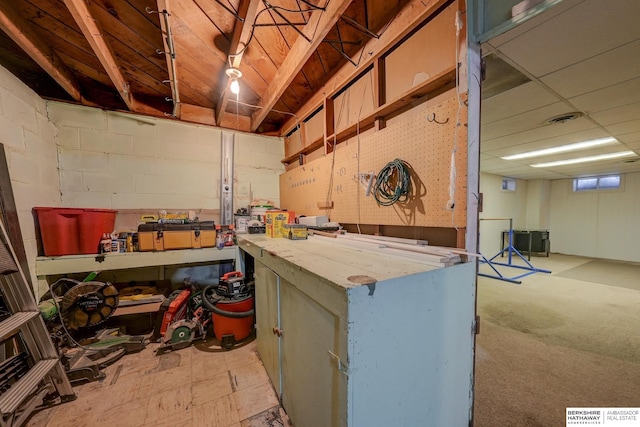 finished basement featuring concrete block wall, visible vents, a drop ceiling, and a workshop area