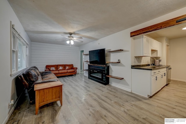 living room with baseboards, ceiling fan, light wood-style flooring, and a textured ceiling