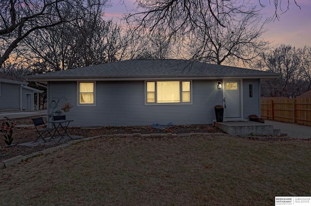 ranch-style home with fence, a lawn, and roof with shingles