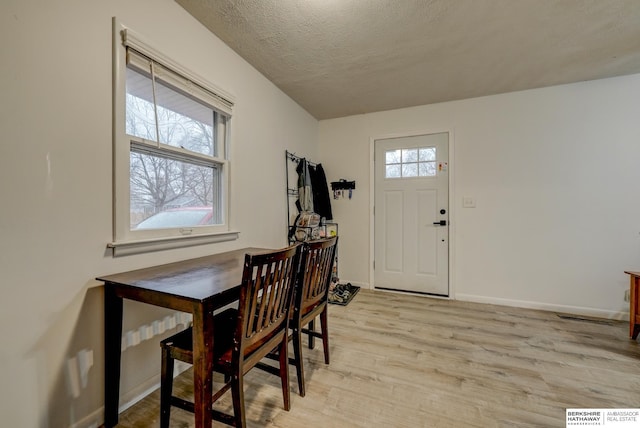 dining area with a textured ceiling, light wood-style floors, baseboards, and a healthy amount of sunlight