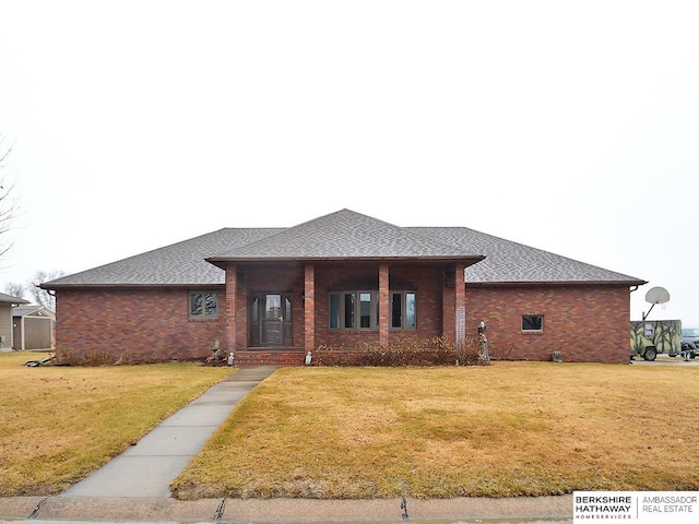 view of front of home featuring brick siding, roof with shingles, and a front yard