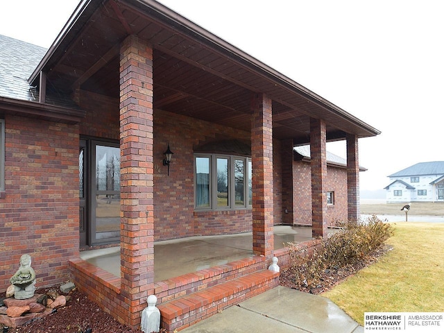 view of exterior entry with brick siding and roof with shingles