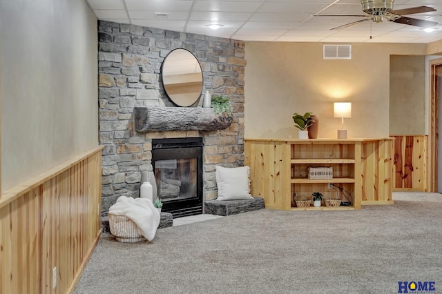 carpeted living area with wainscoting, visible vents, a fireplace, and wood walls