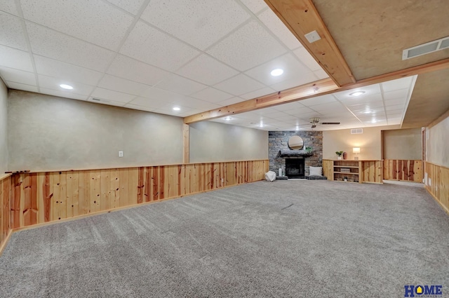 finished below grade area with a wainscoted wall, a stone fireplace, wood walls, and visible vents