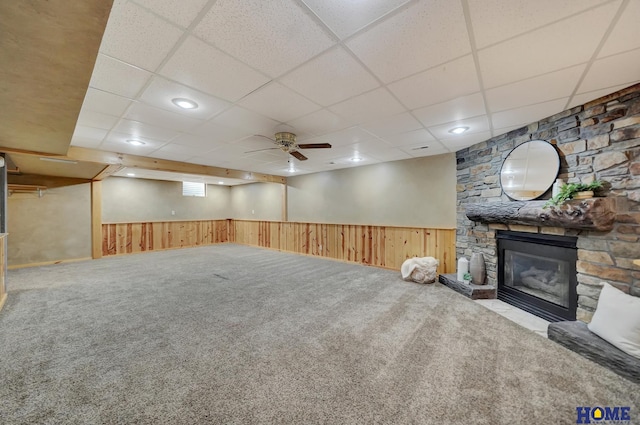 below grade area featuring wooden walls, carpet, a wainscoted wall, and a stone fireplace