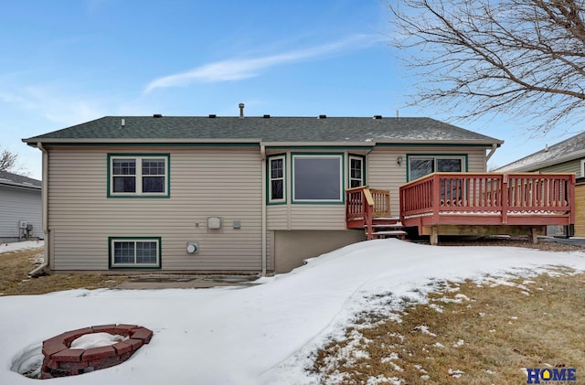 snow covered back of property with a deck, an outdoor fire pit, and a shingled roof