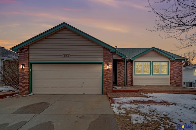 single story home with driveway, central air condition unit, an attached garage, and brick siding