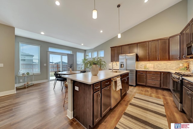 kitchen with light countertops, appliances with stainless steel finishes, light wood-type flooring, tasteful backsplash, and an island with sink