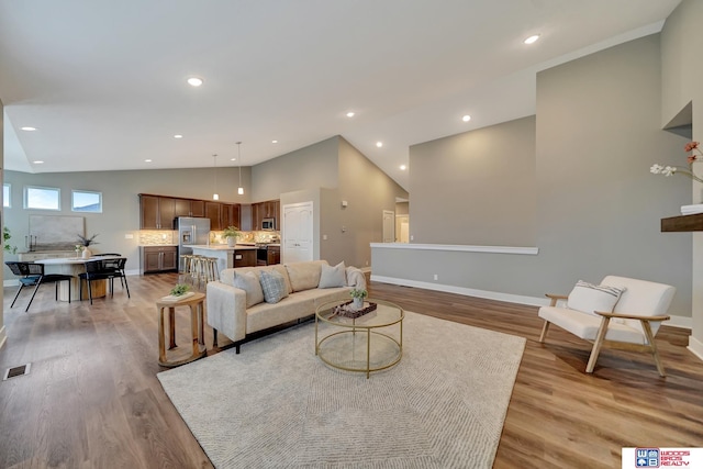 living room featuring high vaulted ceiling, light wood finished floors, recessed lighting, and baseboards