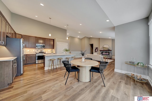 dining room with light wood-style flooring, a fireplace, baseboards, and recessed lighting