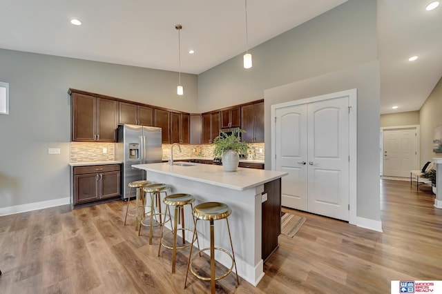 kitchen featuring stainless steel fridge with ice dispenser, light countertops, light wood-style floors, a sink, and a kitchen breakfast bar