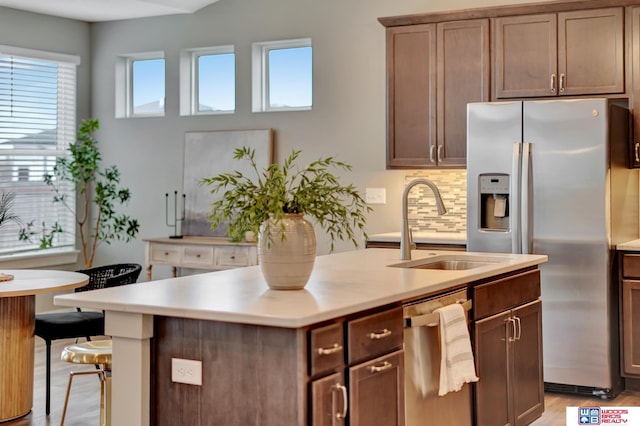 kitchen featuring a sink, light countertops, stainless steel refrigerator with ice dispenser, backsplash, and a center island with sink