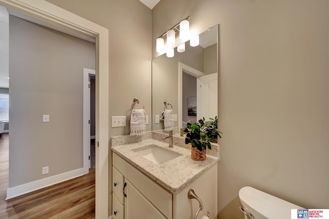 half bathroom featuring baseboards, vanity, toilet, and wood finished floors