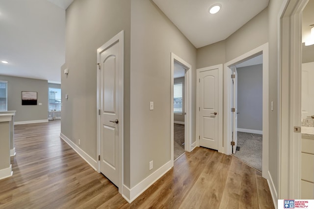 corridor featuring light wood finished floors, baseboards, and a wealth of natural light