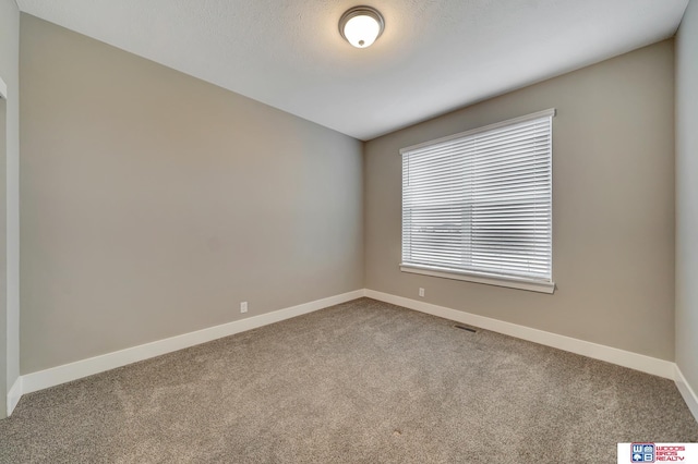 carpeted spare room featuring baseboards, visible vents, and a textured ceiling