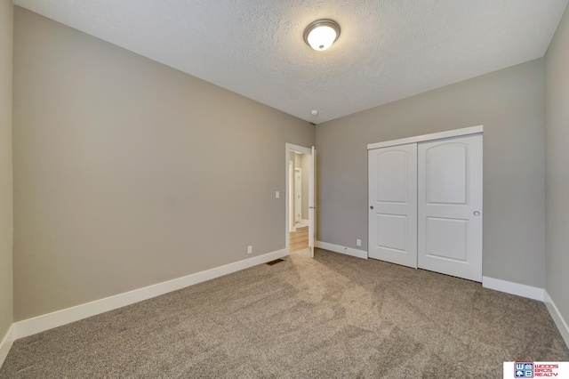 unfurnished bedroom featuring visible vents, baseboards, carpet, a textured ceiling, and a closet