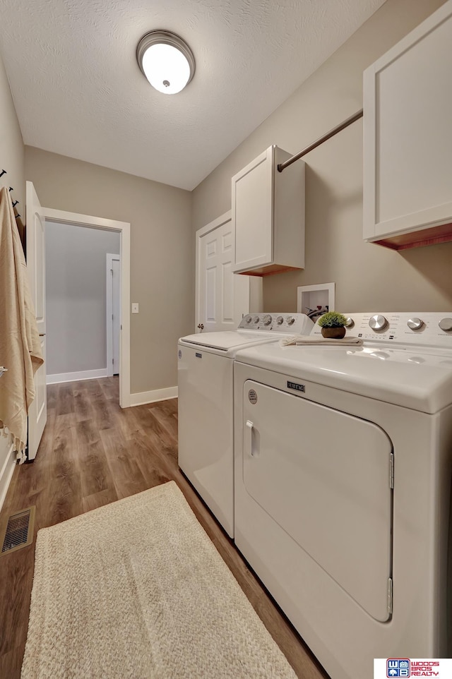 laundry area featuring cabinet space, visible vents, washing machine and dryer, wood finished floors, and baseboards