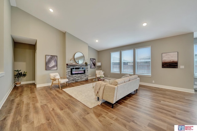 living area featuring high vaulted ceiling, recessed lighting, baseboards, light wood finished floors, and a glass covered fireplace