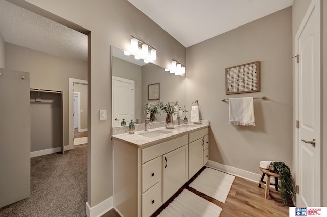 full bath featuring wood finished floors, a sink, baseboards, and double vanity