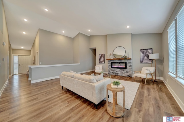 living area with lofted ceiling, recessed lighting, wood finished floors, baseboards, and a glass covered fireplace