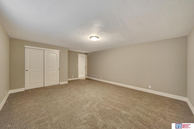 unfurnished bedroom with a textured ceiling, carpet floors, visible vents, baseboards, and a closet