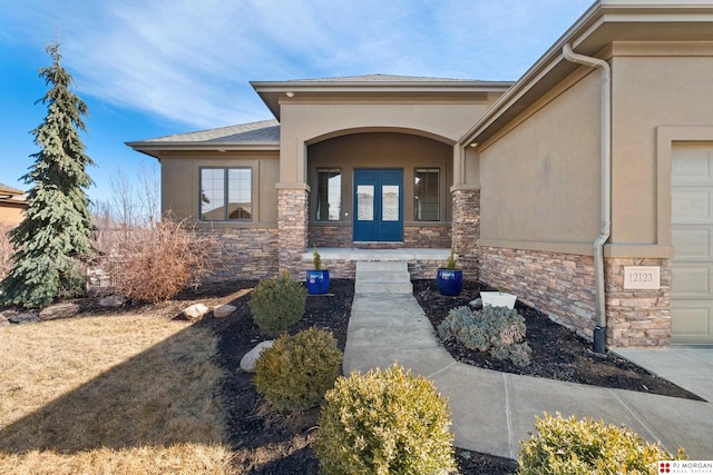 entrance to property featuring a garage, stone siding, and stucco siding