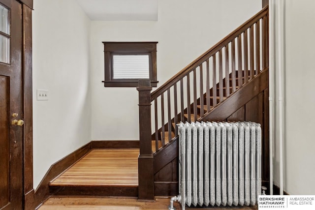 stairway with radiator heating unit, baseboards, and wood finished floors