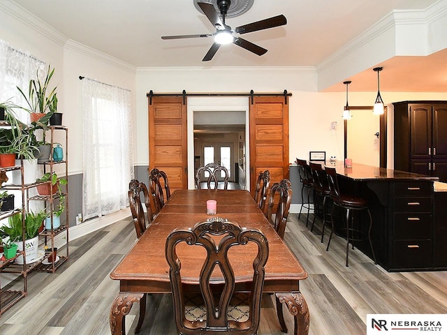 dining room featuring ornamental molding, a barn door, light wood finished floors, and a ceiling fan