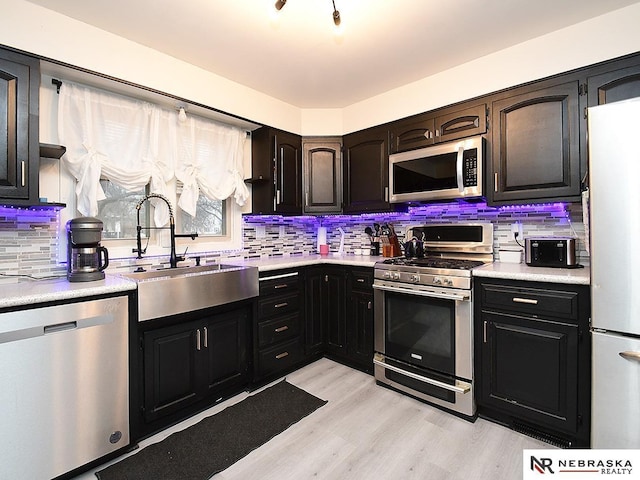 kitchen featuring light wood-style flooring, a sink, light countertops, appliances with stainless steel finishes, and tasteful backsplash