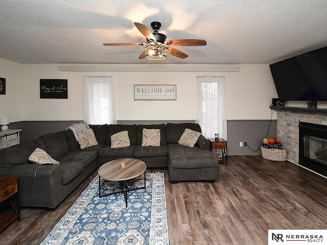 living room featuring a brick fireplace, ceiling fan, a textured ceiling, and wood finished floors