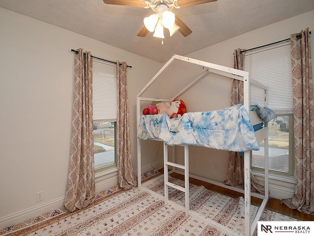 bedroom featuring a ceiling fan, a textured ceiling, baseboards, and wood finished floors