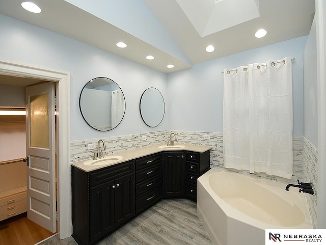 full bathroom featuring double vanity, a garden tub, tile walls, and a sink