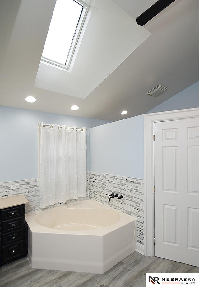 full bathroom featuring a garden tub, tile walls, recessed lighting, wainscoting, and wood finished floors