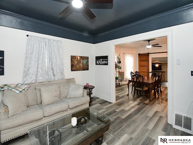 living room featuring a ceiling fan, visible vents, ornamental molding, and wood finished floors