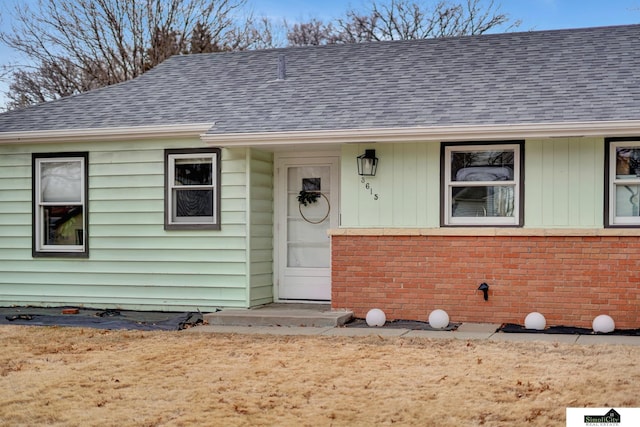 entrance to property featuring brick siding and roof with shingles