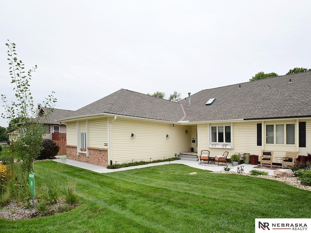 rear view of property with a patio area, a shingled roof, a lawn, and brick siding