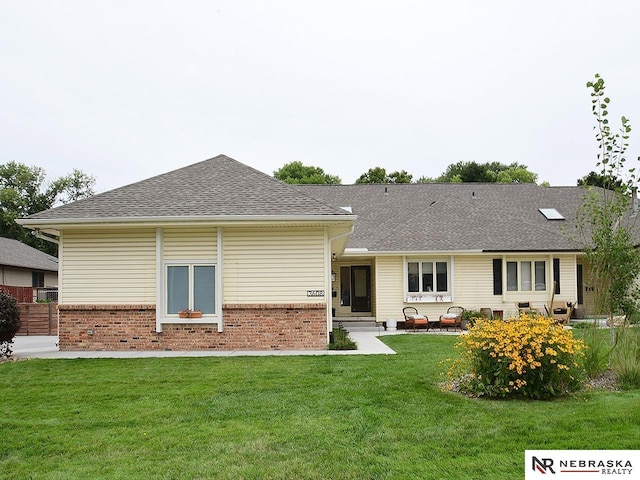 back of property featuring a yard, brick siding, a patio, and a shingled roof