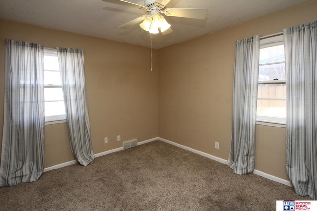 carpeted spare room featuring a wealth of natural light, a ceiling fan, visible vents, and baseboards