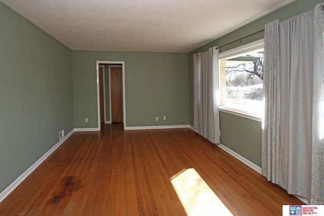 spare room featuring visible vents, baseboards, and wood finished floors