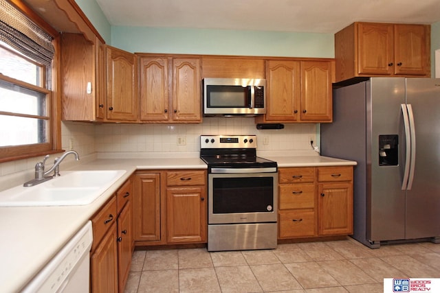 kitchen with brown cabinets, light countertops, backsplash, appliances with stainless steel finishes, and a sink